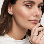 Eine Frau mit einem subtilen Lächeln, die ihr Kinn in einem weißen Top berührt, trägt Tamaris Ohrstecker aus der Silver Love Collection.
