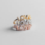 Die Tamaris Ring - Silver Love Collection von Tamaris besteht aus drei Ringen in Gold, Silber und Roségold mit LOVE-Schriftzug und funkelnden Kristall-Akzenten auf grauem Hintergrund.