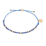 Tamaris Armband mit blauen Natursteinperlen, goldfarbenen Akzenten und größenverstellbarem blauem Textilband.