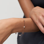 Roségoldfarbenes Damenarmband mit weißen Perlen und floralen Anhängern am Handgelenk einer Frau getragen.