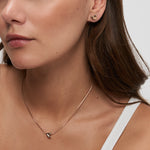 Frau trägt einen kleinen goldenen herzförmigen Ohrstecker und die Halskette Tamaris Halskette - Organic Heart von Tamaris, beide in Gold, vor einem weißen Hintergrund.