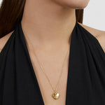 Frau trägt ein schwarzes Neckholder-Top und eine Tamaris Halskette - Heart Amulet von Tamaris, mit einem goldenen herzförmigen Anhänger.