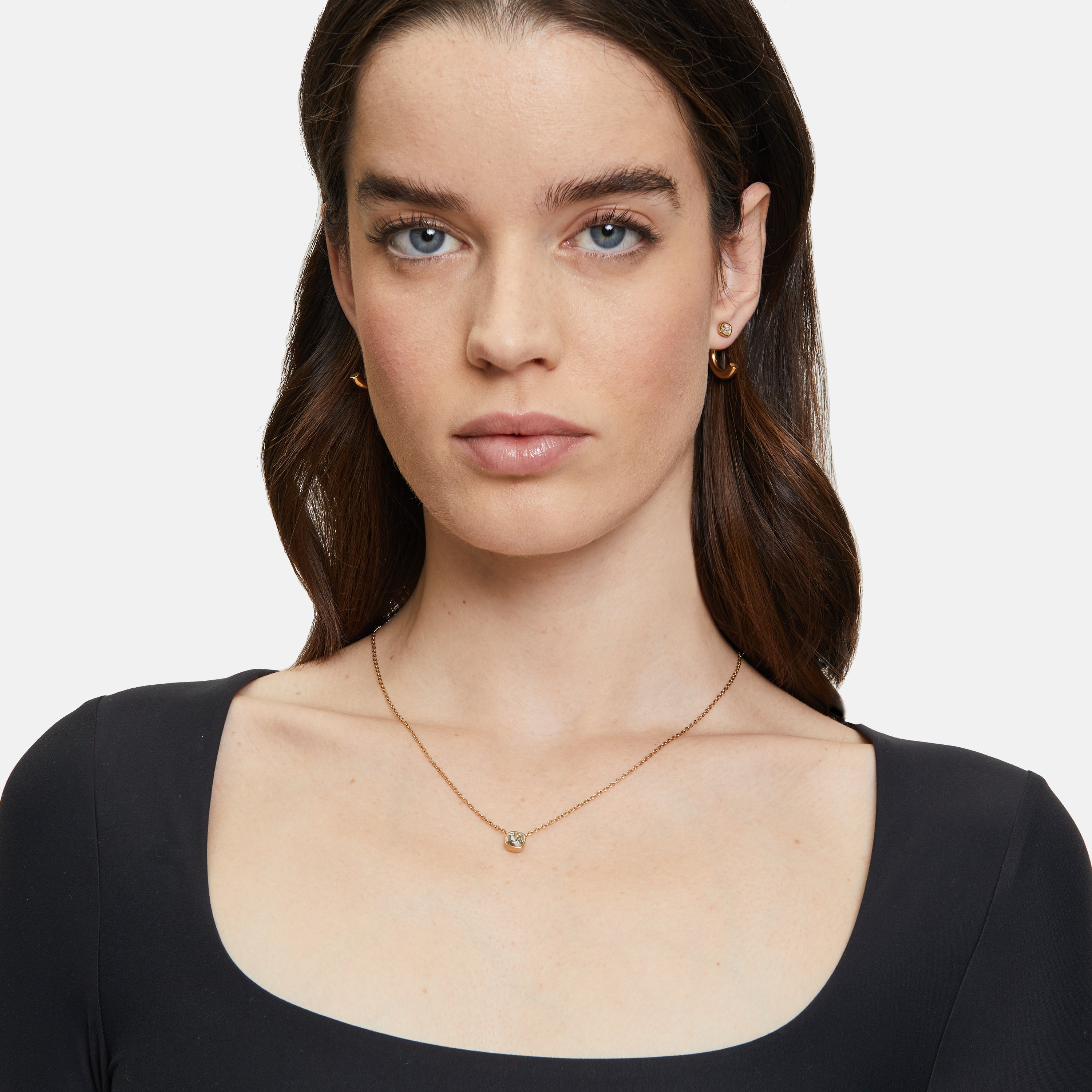 Frau mit langen braunen Haaren trägt ein schwarzes Oberteil mit quadratischem Ausschnitt, goldene Ohrringe und das Tamaris Set - The Layer Collier von Tamaris.