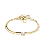 Das Tamaris Set - The Layer von Tamaris besteht aus einem goldenen Kettenarmband mit einem klaren Edelstein in der Mitte und einem verstellbaren Verschluss, der von der Eleganz der Schlangenkette inspiriert ist und auf einem weißen Hintergrund steht.