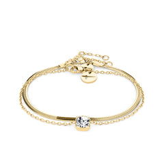 Das Tamaris Set - The Layer von Tamaris besteht aus einem goldenen Kettenarmband mit einem klaren Edelstein in der Mitte und einem verstellbaren Verschluss, der von der Eleganz der Schlangenkette inspiriert ist und auf einem weißen Hintergrund steht.