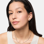 Eine Frau mit langen dunklen Haaren trägt Ohrstecker, eine Tamaris Halskette - Modern Layering und ein weißes Tanktop, während sie in die Kamera schaut.