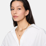 Frau in weißem Hemd trägt die Tamaris Halskette - Modern Layering von Tamaris mit mehrlagigen Goldketten und kleinen goldenen Ohrringen und schaut in die Kamera. Eine perfekte Wahl für Damen Schmuck Fans.