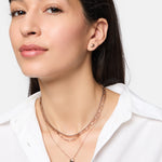 Frau mit langen braunen Haaren trägt die Tamaris Halskette - Modern Layering von Tamaris und ein weißes Button-up-Hemd und posiert selbstbewusst.