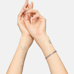 Zwei Hände mit floralen Tattoos tragen ein Tamaris Armband - Modern Layering Armband von Tamaris an einem Handgelenk, posiert vor einem schlichten weißen Hintergrund.