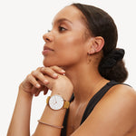 Tamaris Damen Armbanduhr mit roségoldfarbenem Gehäuse, weißem Zifferblatt und senfgelbem Lederarmband am Handgelenk getragen.