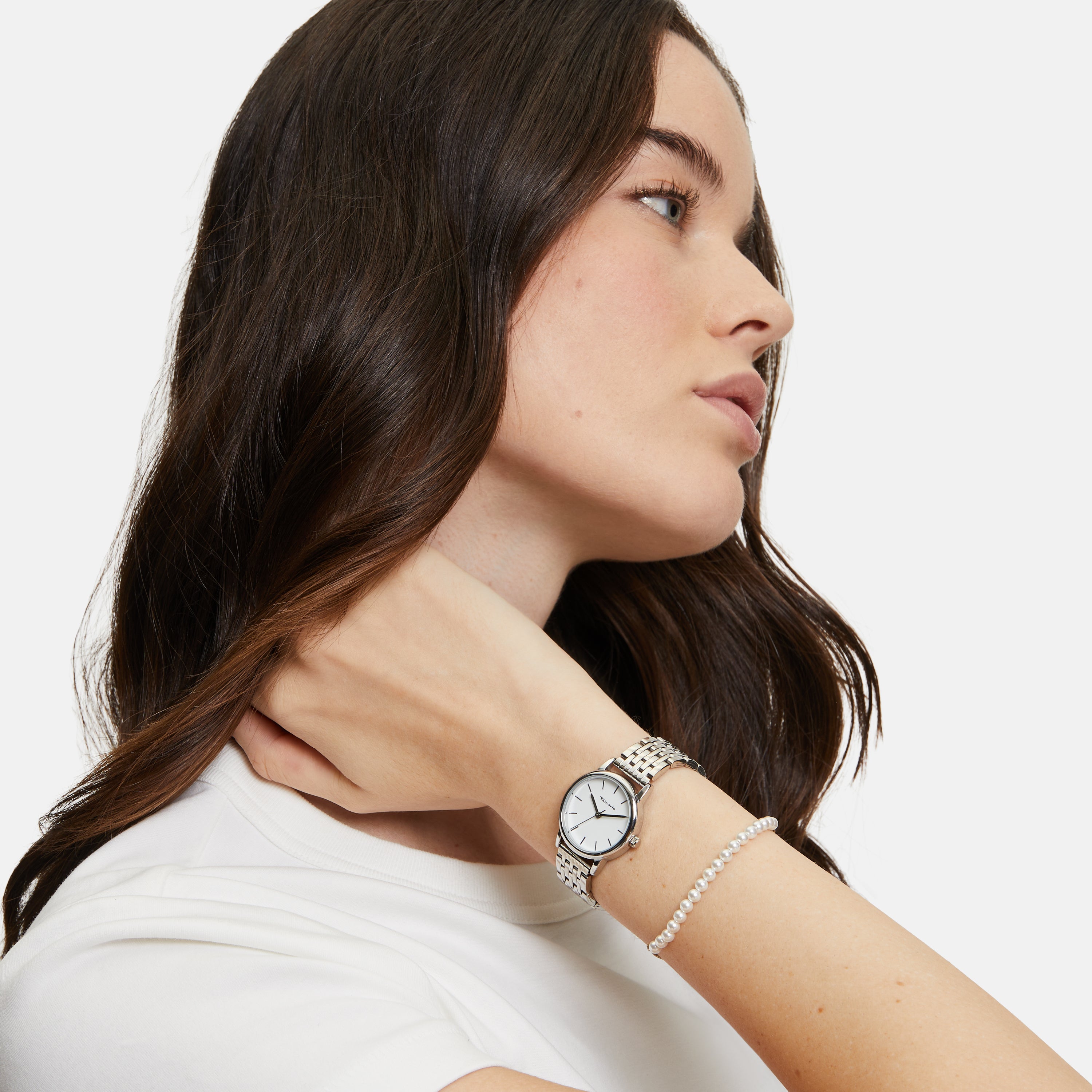Frau in weißem Hemd trägt die Tamaris Armbanduhr - The Small Classic und ein Perlenarmband, wobei sie ihre Hand elegant in den Nacken legt.