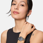 Frau in einem ärmellosen schwarzen Oberteil mit einer Tamaris Armbanduhr - Romantic Flowers und einem goldenen Armband, Hand auf der Schulter.