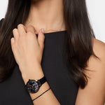 Eine Frau in einem schwarzen Kleid trägt die Tamaris Armbanduhr - Romantic Flowers von Tamaris, deren florales Zifferblatt sichtbar ist, während ihre Hand anmutig auf ihrer Schulter ruht.