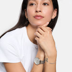 Eine Frau mit weißem Hemd trägt die Tamaris Armbanduhr - Sparkle Up mit elegantem Design und Mesh-Riemen, die mit passendem Schmuck für einen raffinierten Look sorgt, während sie ihr Kinn auf die Hände stützt und zur Seite blickt.