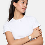 Frau mit dunklen Haaren in einem weißen T-Shirt, Arme verschränkt, trägt die Tamaris Armbanduhr - Sparkle Up von Tamaris mit einem Netzband, schaut zur Seite.