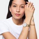 Eine Frau in einem weißen Hemd präsentiert die Tamaris Armbanduhr - Sparkle Up mit Armbändern und sichtbaren Tattoos - ein stilvolles, elegantes Design von Tamaris, das perfekt für den Alltag ist.