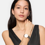 Eine Frau mit langen dunklen Haaren, einem schwarzen ärmellosen Oberteil und kleinen Ohrringen posiert selbstbewusst und trägt die Tamaris Armbanduhr - Sparkle Up by Tamaris mit einem stilvollen Netzband.