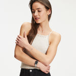 Eine Frau in einem cremefarbenen Strickoberteil und einer schwarzen Hose posiert vor einem weißen Hintergrund und trägt die Tamaris Armbanduhr - The Square von Tamaris für einen klassisch-modernen Stil.