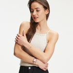 Eine Frau in einem ärmellosen beigen Oberteil und schwarzen Jeans posiert mit verschränkten Armen und präsentiert die Tamaris Armbanduhr - The Square mit ihrem eleganten Edelstahlband, während sie zur Seite schaut.