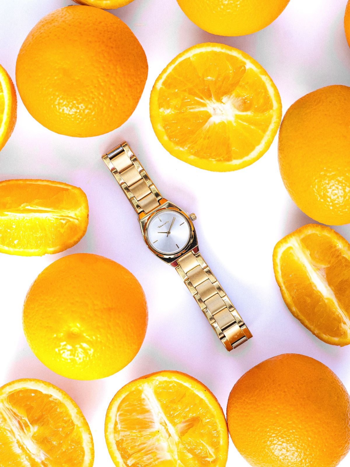 Tamaris Damenuhr ‚The Cool One‘ in Gold zwischen frischen Orangen auf hellem Hintergrund.