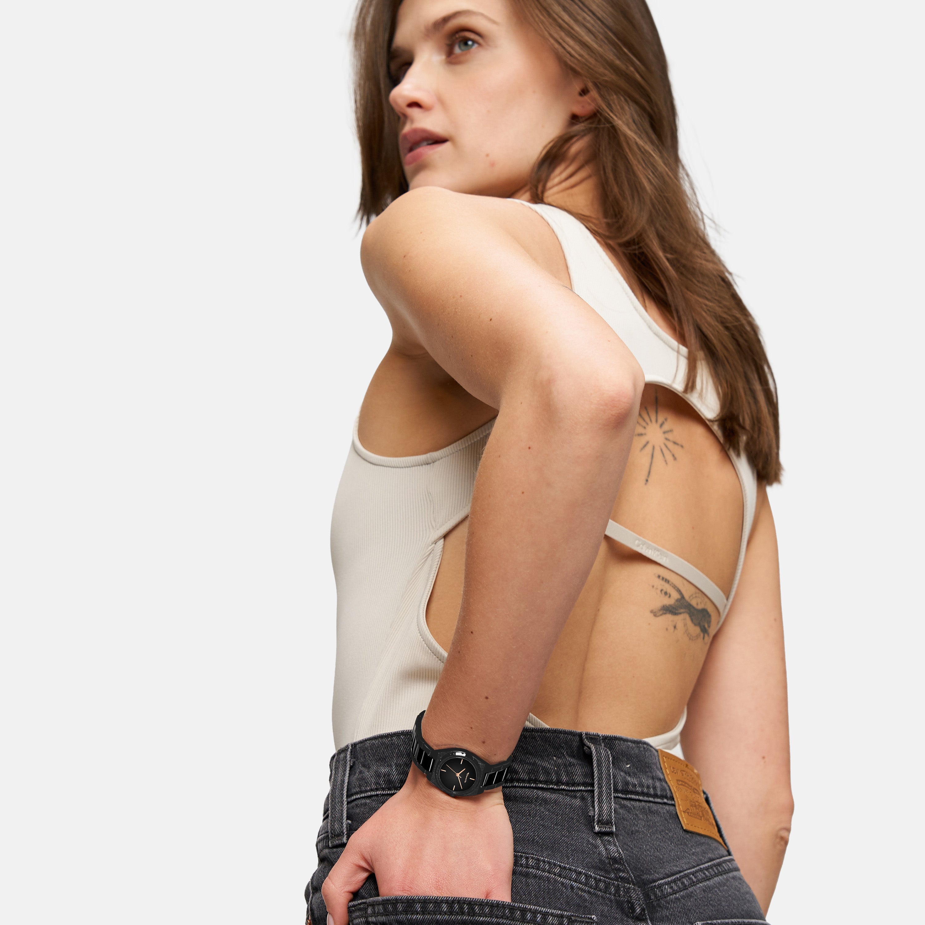 Eine Frau in ärmellosem Top und schwarzer Jeans, die Hand in der Gesäßtasche, modelliert die Tamaris Armbanduhr - The Cool One by Tamaris: eine Damenuhr aus Edelstahl, die minimalistisches Design verkörpert.