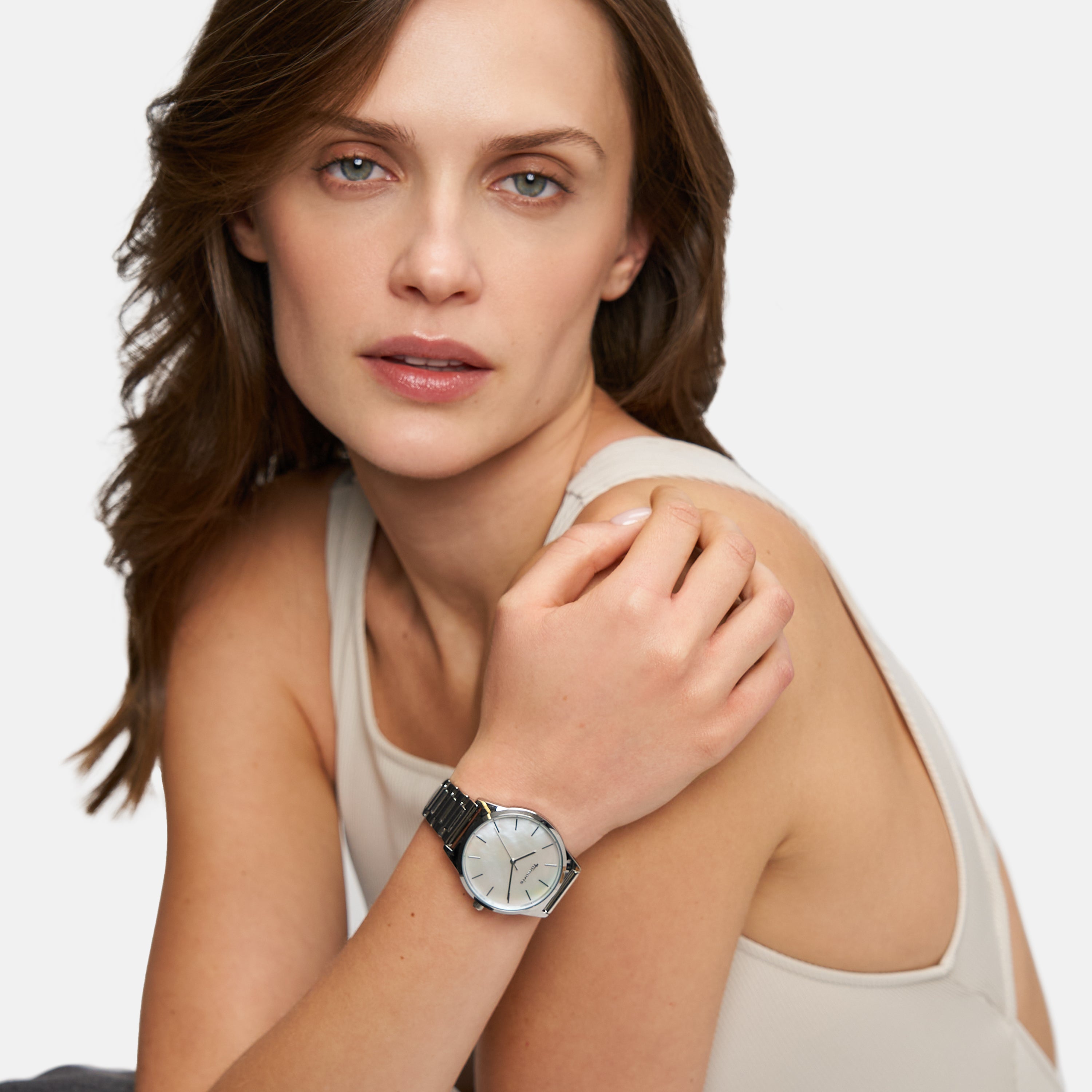 Eine Frau in einem beigen Tank-Top modelliert die Tamaris Armbanduhr - Basic Elegance mit einem eleganten Perlmuttzifferblatt und blickt in die Kamera vor einem schlichten Hintergrund.