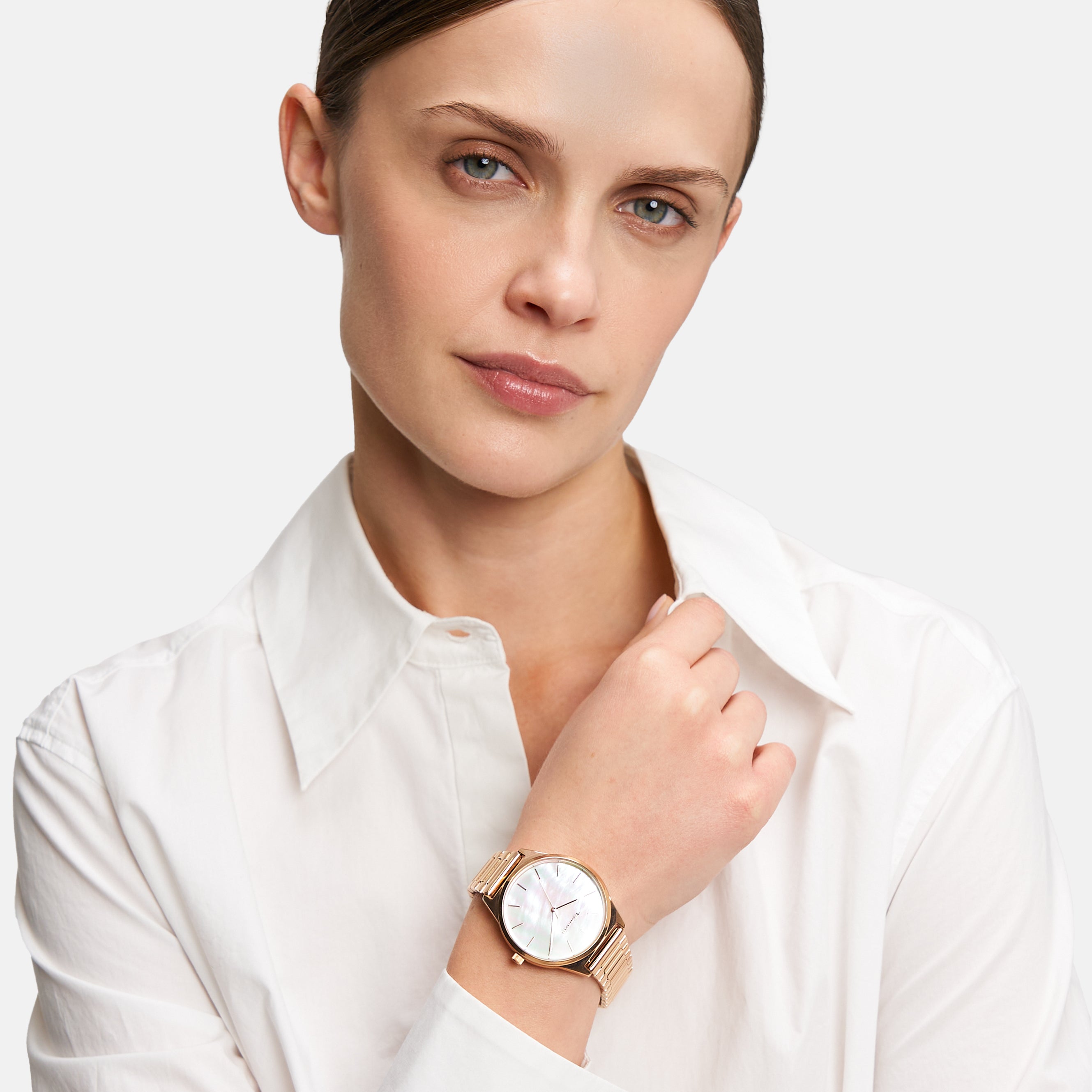 Frau in weißem Hemd, die eine Tamaris Armbanduhr - Basic Elegance mit Perlmutt-Zifferblatt trägt und mit neutralem Blick in die Kamera schaut.