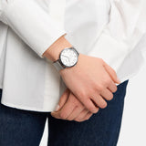 Eine Person in weißem Hemd und Jeans trägt die stilvolle Tamaris Armbanduhr - Clover, eine silberne Tamaris-Uhr mit weißem Zifferblatt und elegantem Netzband.