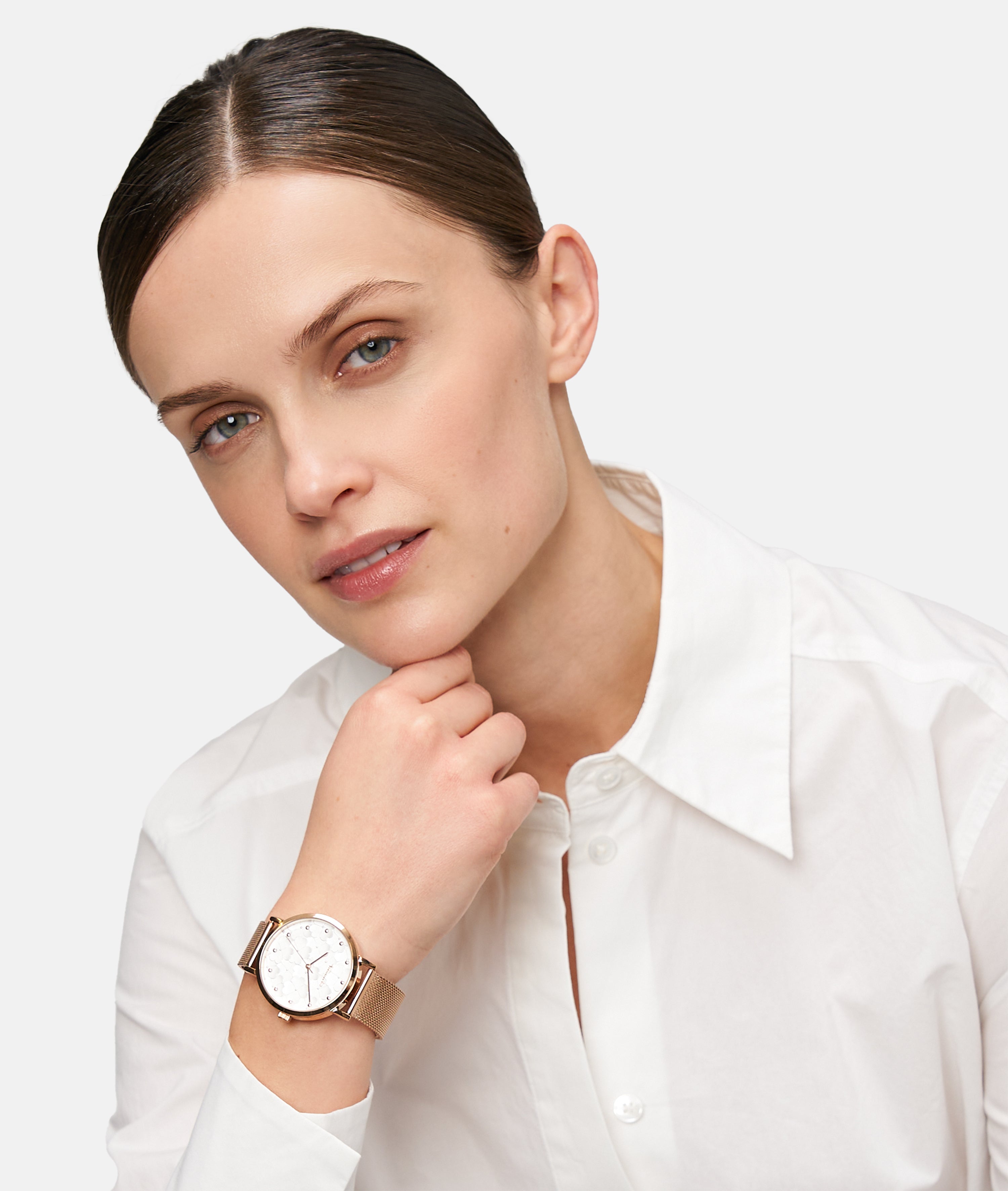 Frau in weißem Hemd stützt ihr Kinn auf die Hand, trägt die stylische Tamaris Armbanduhr - Clover von Tamaris mit Netzband und schaut in die Kamera.