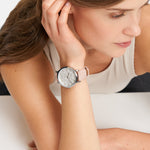 Eine Frau in einem ärmellosen Top stützt ihren Kopf auf die Hand und trägt die Tamaris Armbanduhr - Clover mit floralem Zifferblatt und stilvollem rosa Lederband von Tamaris am Handgelenk.
