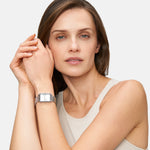 Eine Frau in einem ärmellosen Oberteil posiert elegant mit vor dem Gesicht verschränkten Händen und präsentiert dabei die Tamaris Armbanduhr - Square Meets Mesh von Tamaris.
