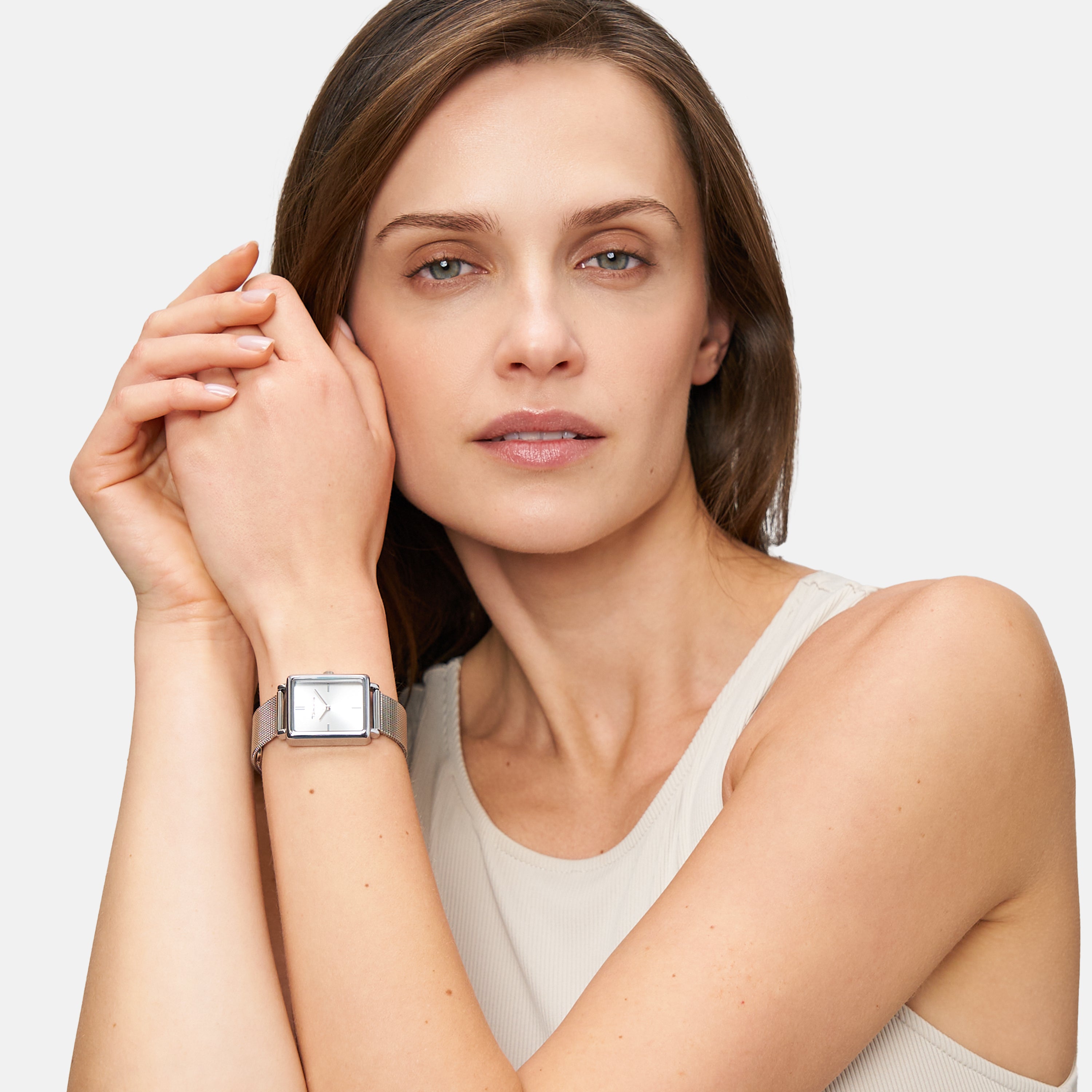 Eine Frau in einem ärmellosen Oberteil posiert elegant mit vor dem Gesicht verschränkten Händen und präsentiert dabei die Tamaris Armbanduhr - Square Meets Mesh von Tamaris.