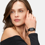 Frau trägt ein schwarzes schulterfreies Oberteil und eine modische Tamaris Armbanduhr - Square Meets Mesh von Tamaris, mit Blick zur Seite.