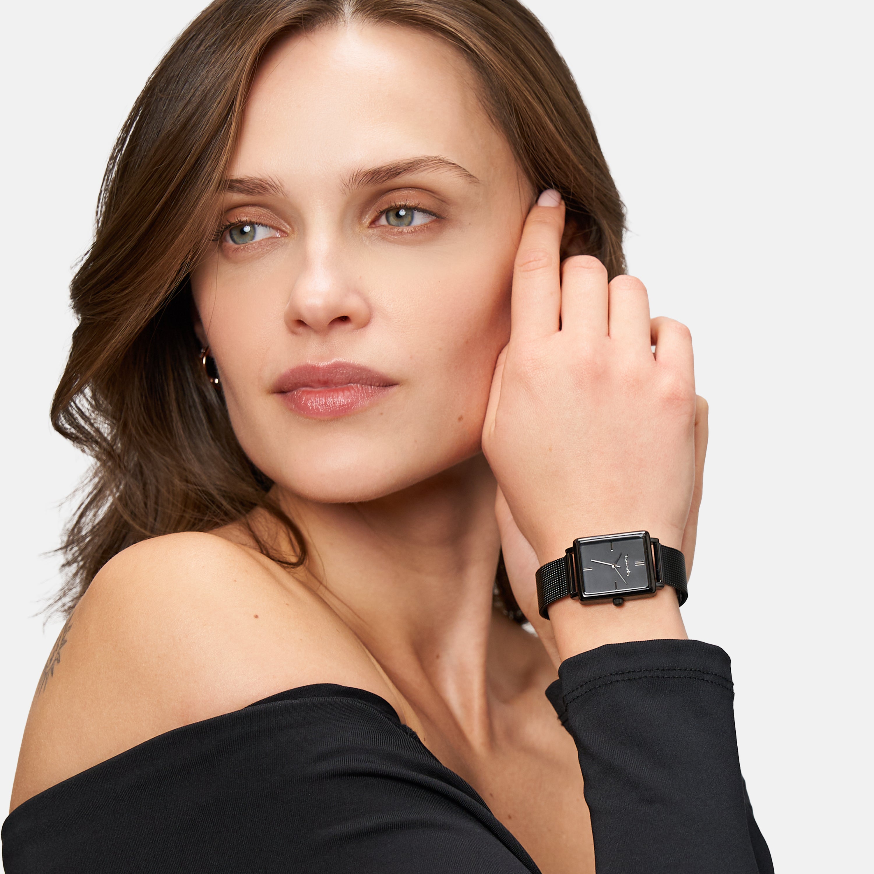 Frau trägt ein schwarzes schulterfreies Oberteil und eine modische Tamaris Armbanduhr - Square Meets Mesh von Tamaris, mit Blick zur Seite.