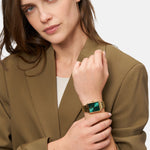 Eine Frau in einem braunen Blazer präsentiert die Tamaris Armbanduhr - The Bicolor Square mit Edelstahlarmband und auffallend grünem Zifferblatt und blickt selbstbewusst in die Kamera.