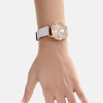 Eine Hand trägt die Tamaris Armbanduhr - The Flower: eine stilvolle Uhr mit Goldgehäuse von Tamaris mit weißem Silikonband und einem eleganten Blumenprint auf dem Zifferblatt.