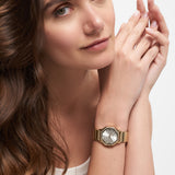 Frau mit langen braunen Haaren trägt eine Tamaris Sparkling Octavia Armbanduhr mit schimmernden Zirkoniasteinen und goldenem Edelstahlband, die Hände sanft in ihrem weißen Tanktop verschränkt.