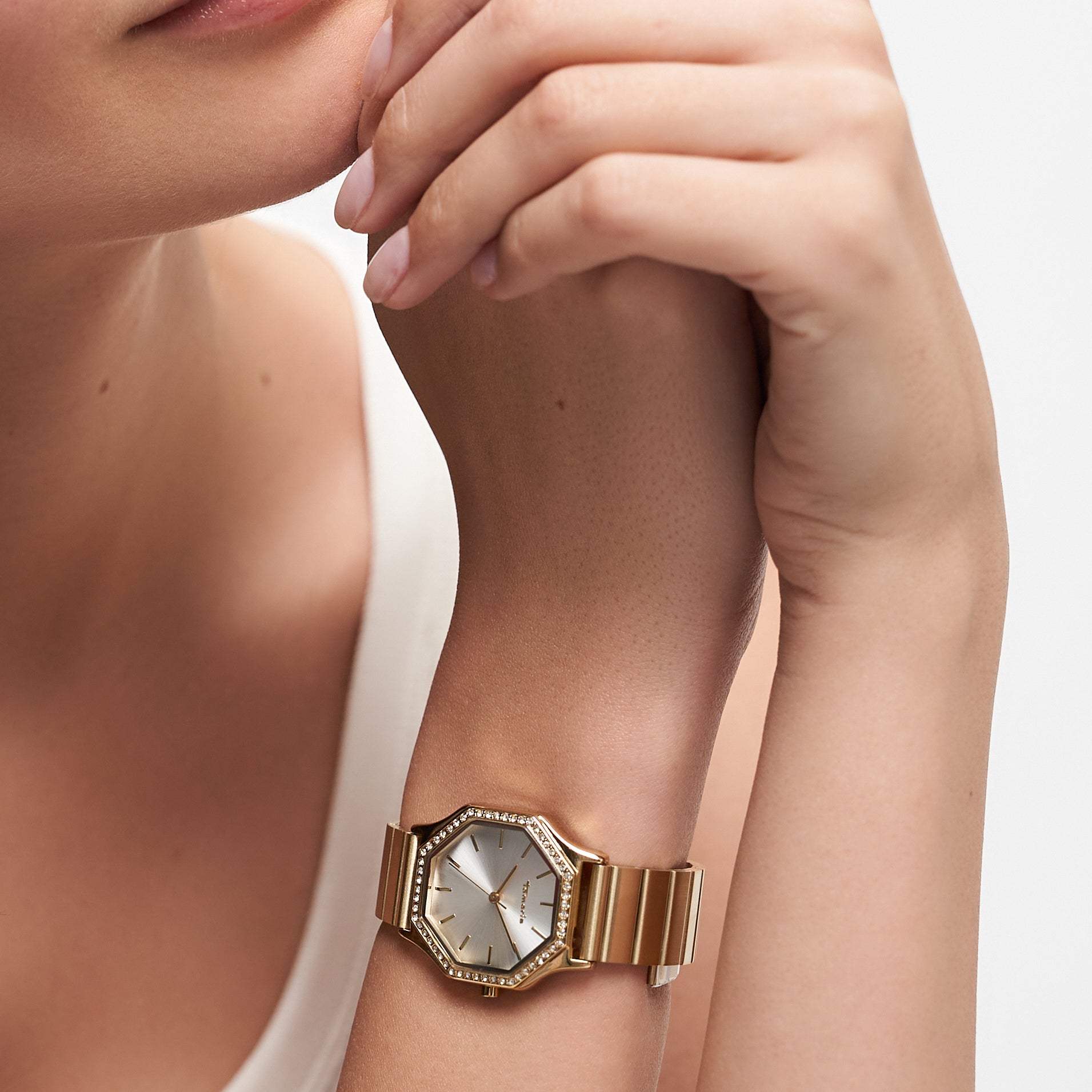 Eine Frau, die die Tamaris Armbanduhr - Sparkling Octavia mit einem goldenen sechseckigen Gesicht, Zirkoniasteinen und einem eleganten Edelstahlarmband trägt, stützt ihre Hand auf ihr Kinn.
