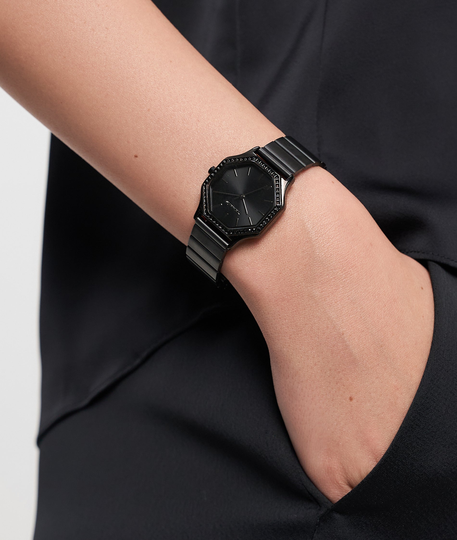 Person trägt eine Tamaris Sparkling Octavia Armbanduhr mit sechseckigem Zifferblatt und schwarzem Armband, Hand in der Tasche.