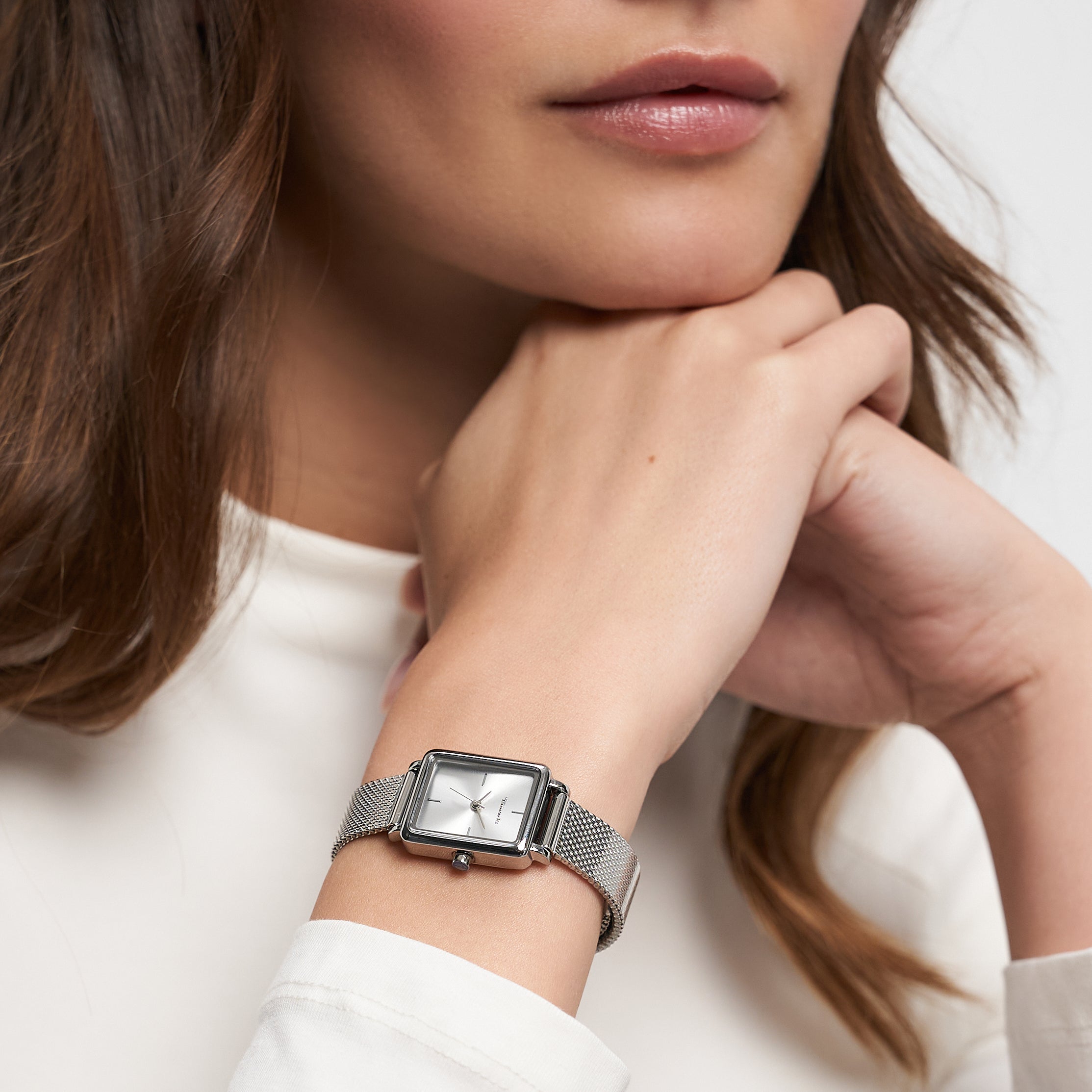 Eine Frau in einem weißen langärmeligen Oberteil, die die Tamaris Armbanduhr - Tiny Watch trägt, stützt ihr Kinn auf ihre Hände - ein Bild von minimalistischer Eleganz.