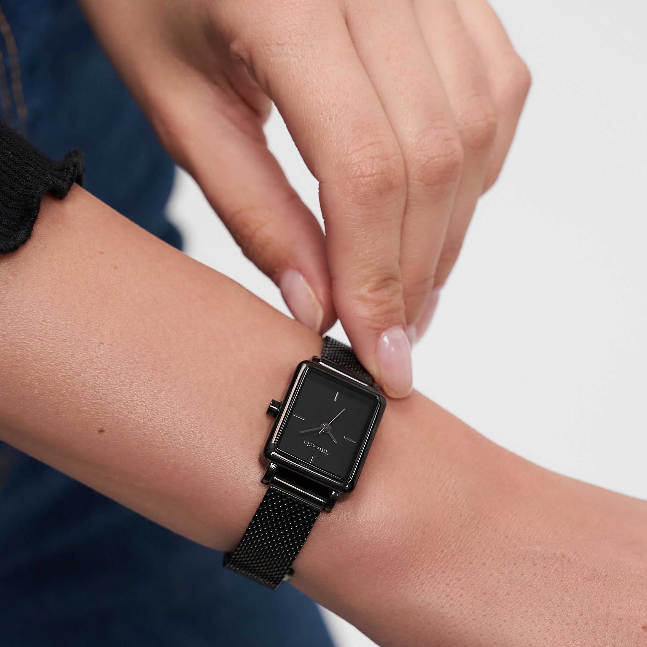 Eine Person trägt eine schwarze, quadratische Tamaris Armbanduhr - Tiny Watch von Tamaris an ihrem linken Handgelenk und unterstreicht damit die minimalistische Eleganz.