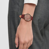 Eine Person, die eine Tamaris Armbanduhr - Stamped Flowers mit Lederband und eine graue Hose trägt, den Arm entspannt an der Seite.