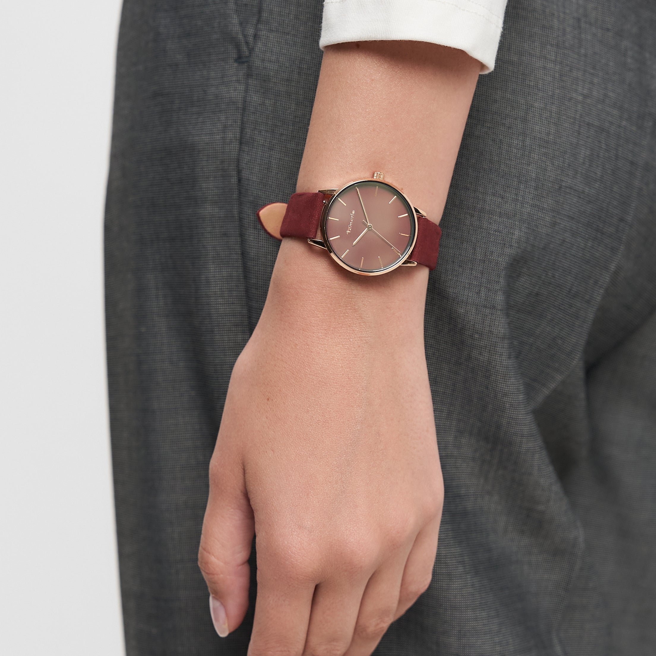 Eine Person, die eine Tamaris Armbanduhr - Stamped Flowers mit Lederband und eine graue Hose trägt, den Arm entspannt an der Seite.