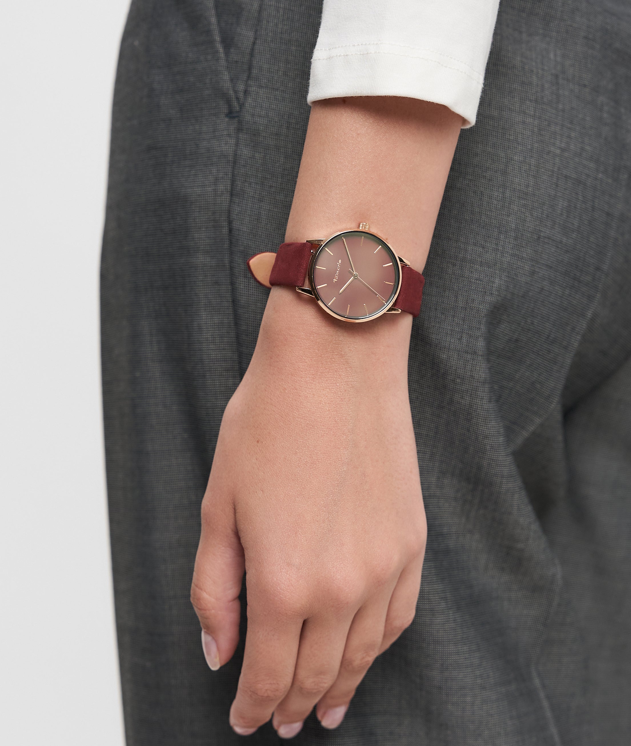 Eine Person, die eine Tamaris Armbanduhr - Stamped Flowers mit Lederband und eine graue Hose trägt, den Arm entspannt an der Seite.