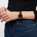 Eine Person, die eine Tamaris Armbanduhr - Stamped Flowers, ein schwarzes langärmeliges Oberteil und eine blaue Jeans trägt.