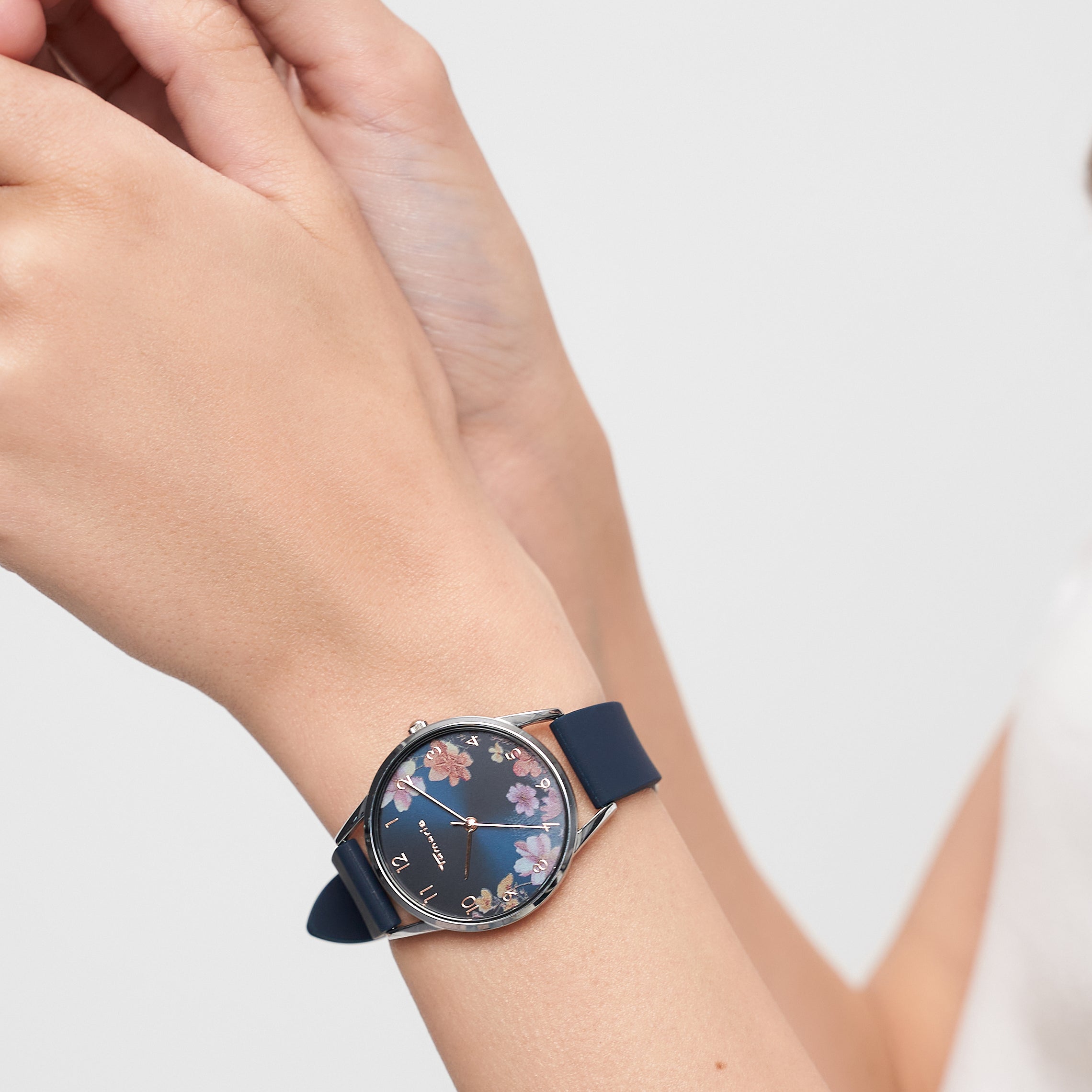 Eine Person, die eine Tamaris Armbanduhr - Sporty Flowers von Tamaris trägt, stellt die blaue Blumenuhr mit sportlichem Silikonband an ihrem linken Handgelenk ein.