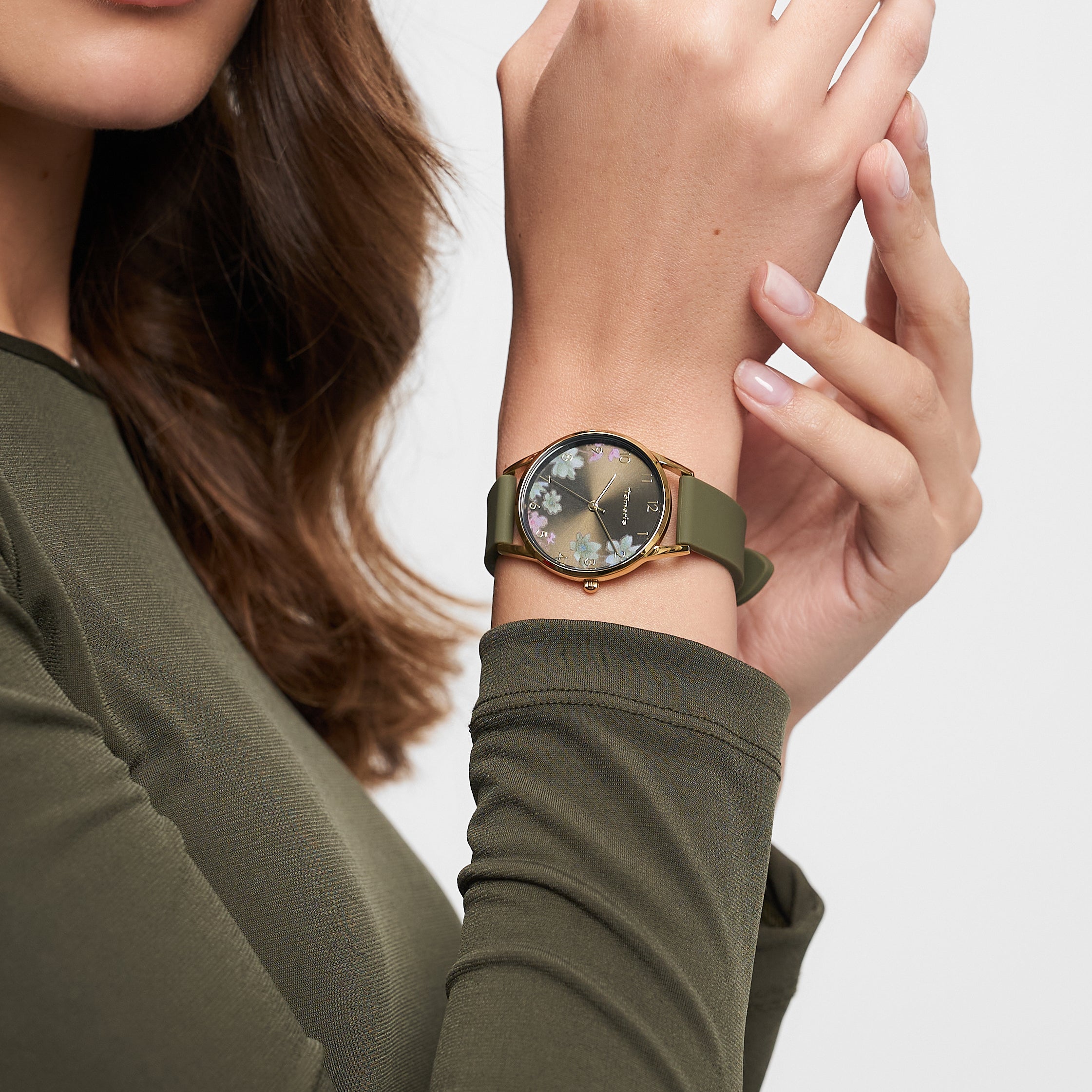 Eine Frau trägt ein olivgrünes langärmeliges Oberteil und eine Tamaris Armbanduhr - Sporty Flowers von Tamaris mit Blumenmotiv und grünem Silikonband am Handgelenk.
