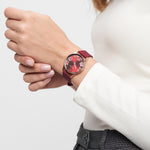 Die Person trägt eine Tamaris Armbanduhr - Sporty Flowers von Tamaris mit Blumenmotiv und Silikonband, ein weißes Oberteil und eine graue Hose.