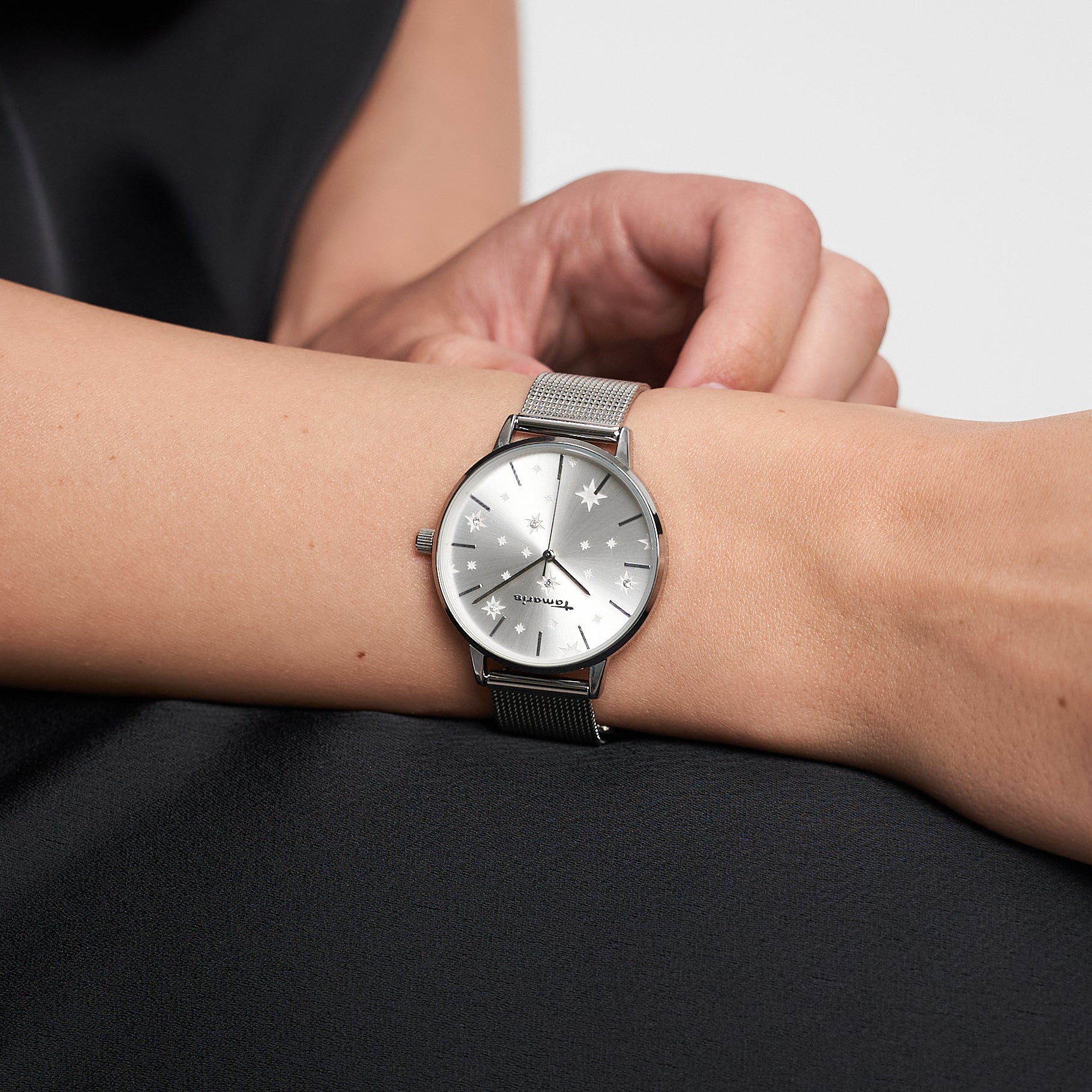 Die Tamaris Armbanduhr - Shiny Stars von Tamaris verleiht mit ihrem silbernen Netzband einem schwarzen Outfit einen Hauch von Eleganz und modernem Stil.