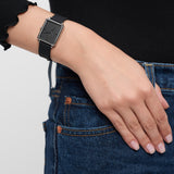 Eine Person, die die Tamaris Armbanduhr - The Silicon Square von Tamaris mit schwarzem Silikonband und blauer Jeans trägt, stützt ihre Hand auf die Hüfte.